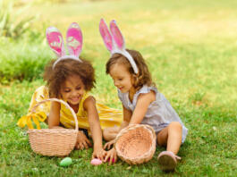 two girls are sitting on the lawn and putting Easter eggs in baskets