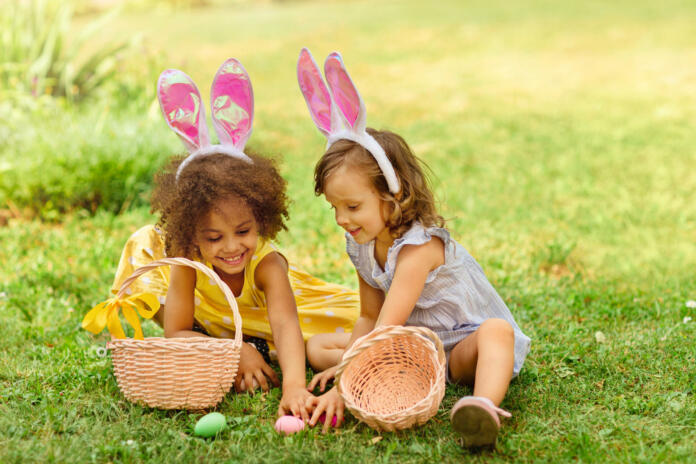 two girls are sitting on the lawn and putting Easter eggs in baskets
