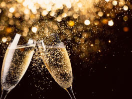 Two glasses of champagne toasting in the nigh with lights bokeh, glitter and sparks on the background