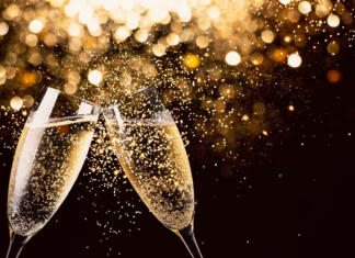 Silvestrovanje malo drugače Two glasses of champagne toasting in the nigh with lights bokeh, glitter and sparks on the background