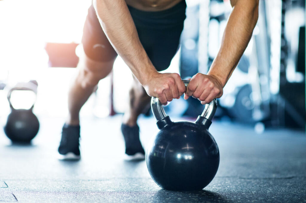 Unrecognizable young fit man doing strength training, doing push ups on kettlebells in modern gym.