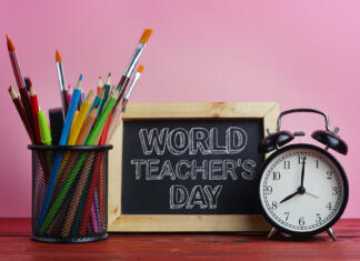 Zanimivosti o učiteljih v Sloveniji – število učiteljev v Sloveniji in še World Teacher's Day Text. Blackboard, Alarm Clock and School Stationary in Basket on Wooden Table Pink Background