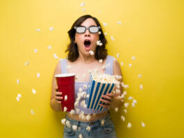 Wow! Surprised young woman throwing her popcorn while watching an exciting action movies at the cinema