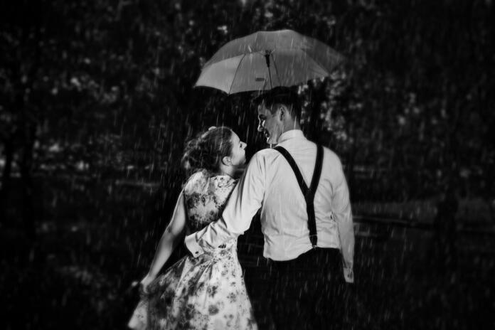 Young romantic couple in love flirting in rain, man holding umbrella. Dating, romance, black and white