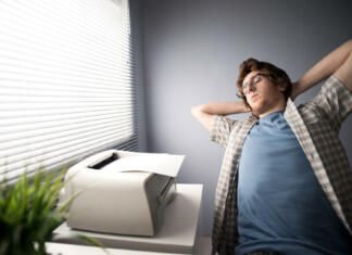 Ali kot študent potrebujem tiskalnik? Young tired man relaxing and stretching at workplace.