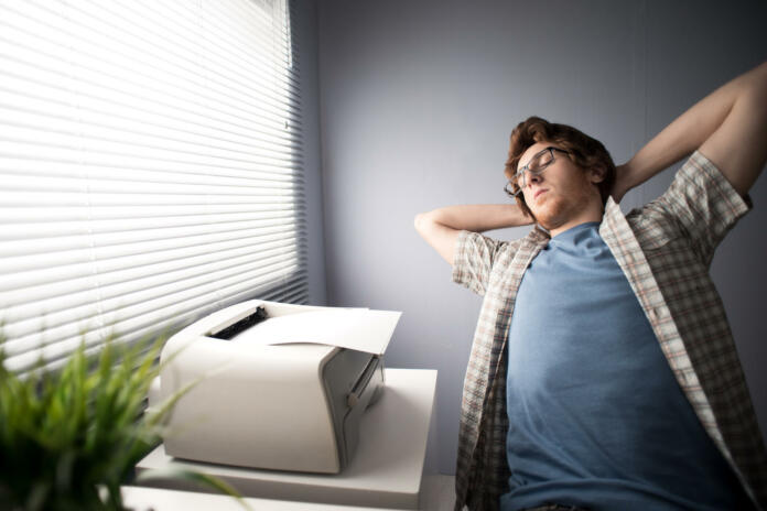 Young tired man relaxing and stretching at workplace.