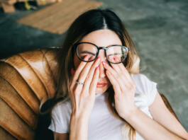 Young woman rubs her eyes after using glasses. Eye pain or fatigue concept.