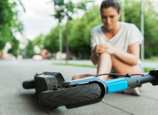 Vse več je poškodb zaradi e-skirojev Young woman suffering from knee pain after e-scooter riding accident on a city street