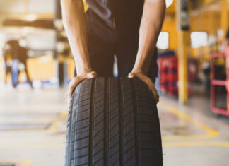 Znaš skrbeti za svoje pnevmatike? A handsome young mechanic in white gloved uniform is putting his hand on a new tire and checking and checking the condition of the tire while doing car service.
