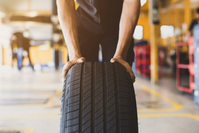 A handsome young mechanic in white gloved uniform is putting his hand on a new tire and checking and checking the condition of the tire while doing car service.