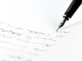 Black fountain pen is writing a letter or a manuscript on a white paper, copy space, close-up shot with selected focus and narrow depth of field