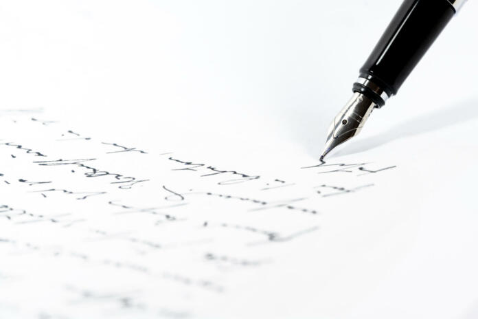 Black fountain pen is writing a letter or a manuscript on a white paper, copy space, close-up shot with selected focus and narrow depth of field