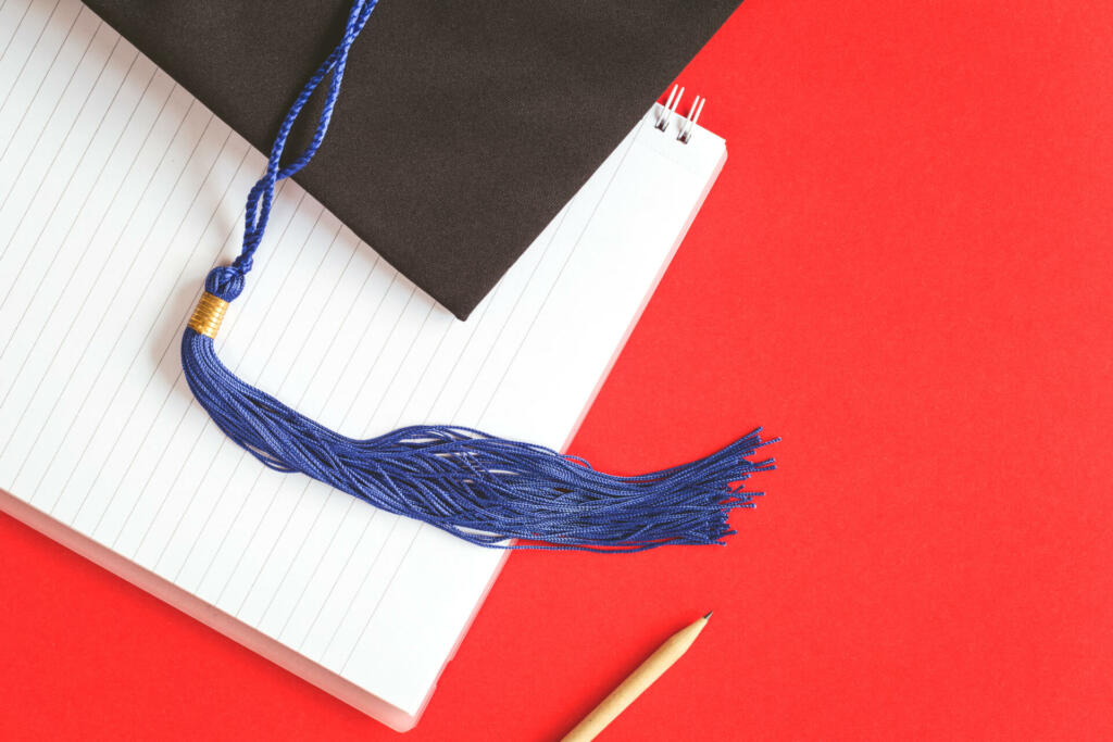 Black Graduation Cap with notebook on red background. Masters or Bachelors Degree thesis writing. Knowledge qualifications and higher education with copy space