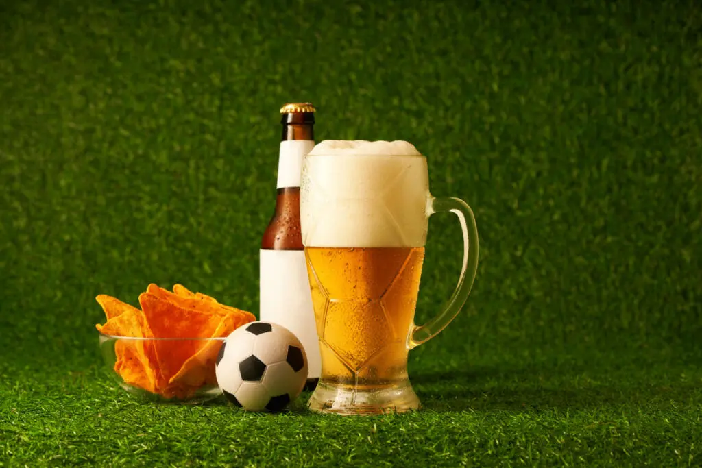Bottle and glass of beer on the green grass background. Football fan concept