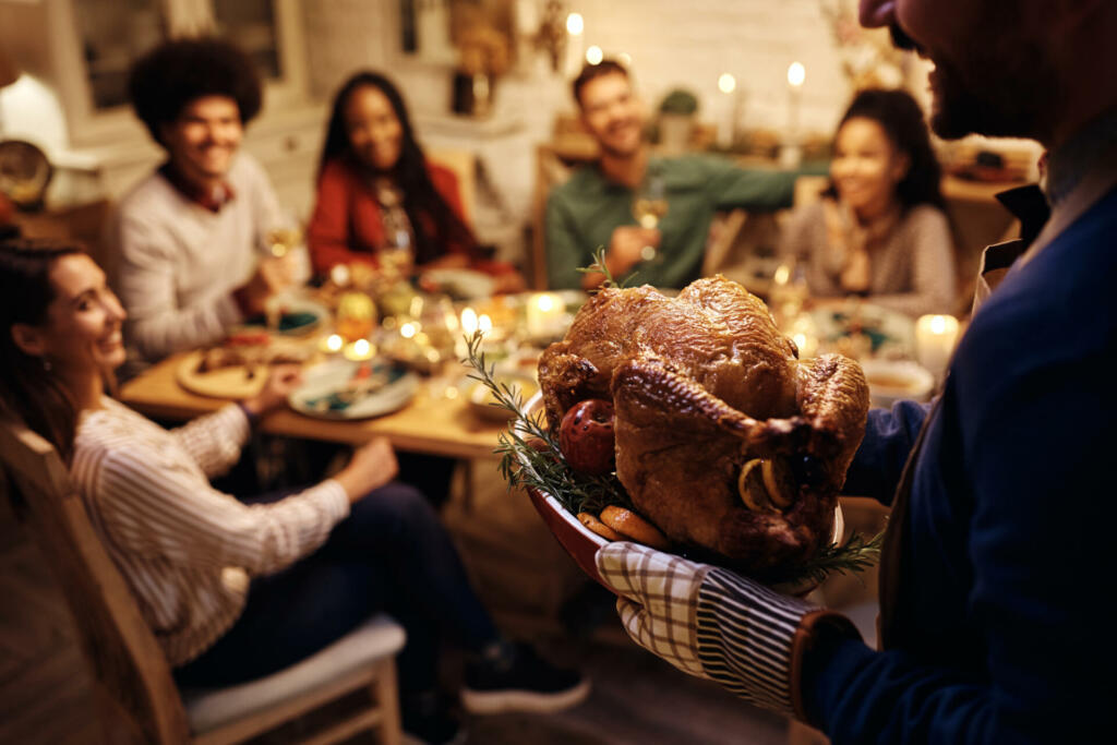 Close up of man serving Thanksgiving turkey to his friend during a meal at dining table.