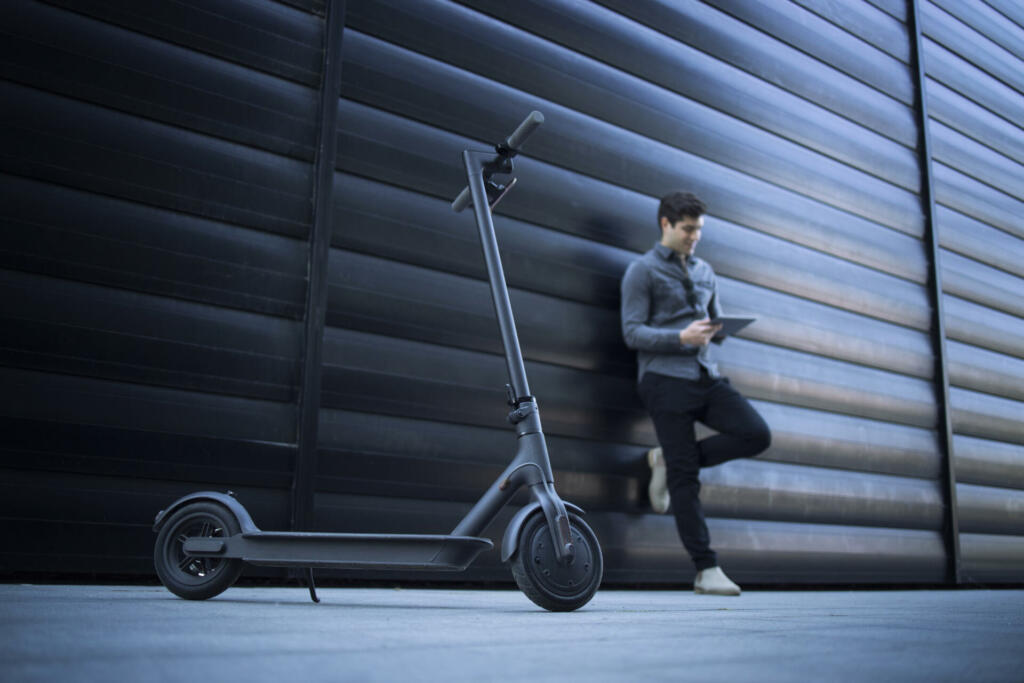Electric scooter. Eco friendly modern way of transportation. In background handsome business person caucasian man using tablet computer leaning on black business building.