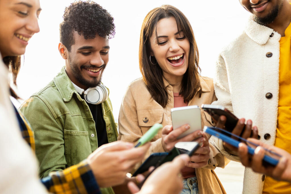 Happy group of young friends using smartphone in the street - Millennial generation people having fun sharing content in social media platform app outdoors - Technology, friendship and youth concept