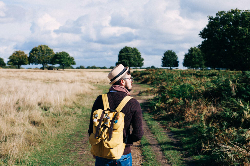 Man with backpack walking on pathway between field at daytime