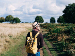 Man with backpack walking on pathway between field at daytime