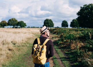 Kako potovati sam? Man with backpack walking on pathway between field at daytime