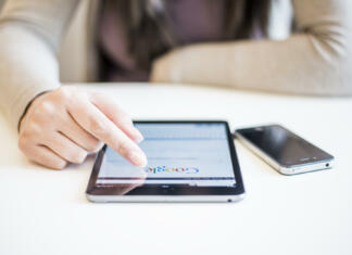 Google vrnil nizek udarec Applu z Google Messages Novi Sad, Serbia - October 6, 2014: Woman's hands Googling on electronic device.Woman hands holding and touching on Apple iPad mini with Google search web page on a screen.