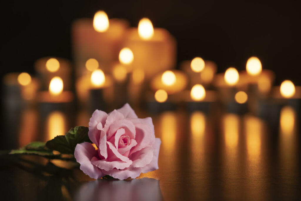 PINK ROSE ON THE GRAVE AND LIGHTED CANDLES UNFOCUSED IN THE BACKGROUND.