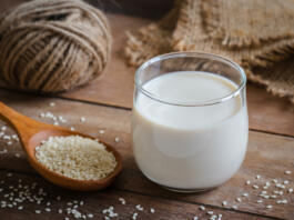 Sesame milk in glass and white sesame seeds on wooden spoon