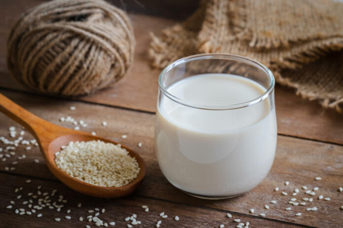Sesame milk in glass and white sesame seeds on wooden spoon