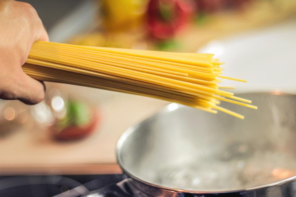 Oseba v rokah drži špagete nad posodo z vrelo vodo