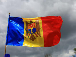 Zastava (od leve proti desni: modra, rumena, rdeča; na sredini grb) plapola v zraku