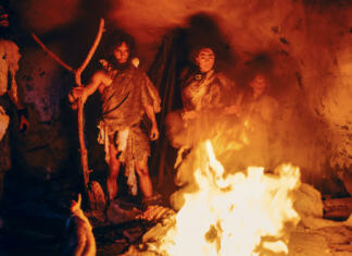 Tribe of Prehistoric Hunter-Gatherers Wearing Animal Skins Stand Around Bonfire Outside of Cave at Night. Portrait of Neanderthal / Homo Sapiens Family Doing Pagan Religion Ritual Near Fire