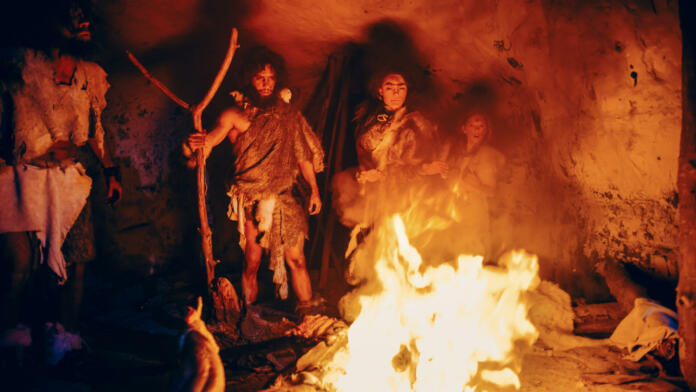 Tribe of Prehistoric Hunter-Gatherers Wearing Animal Skins Stand Around Bonfire Outside of Cave at Night. Portrait of Neanderthal / Homo Sapiens Family Doing Pagan Religion Ritual Near Fire