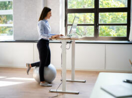 Woman Using Adjustable Height Standing Desk In Office For Good Posture