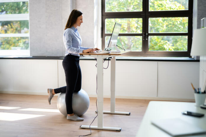 Woman Using Adjustable Height Standing Desk In Office For Good Posture