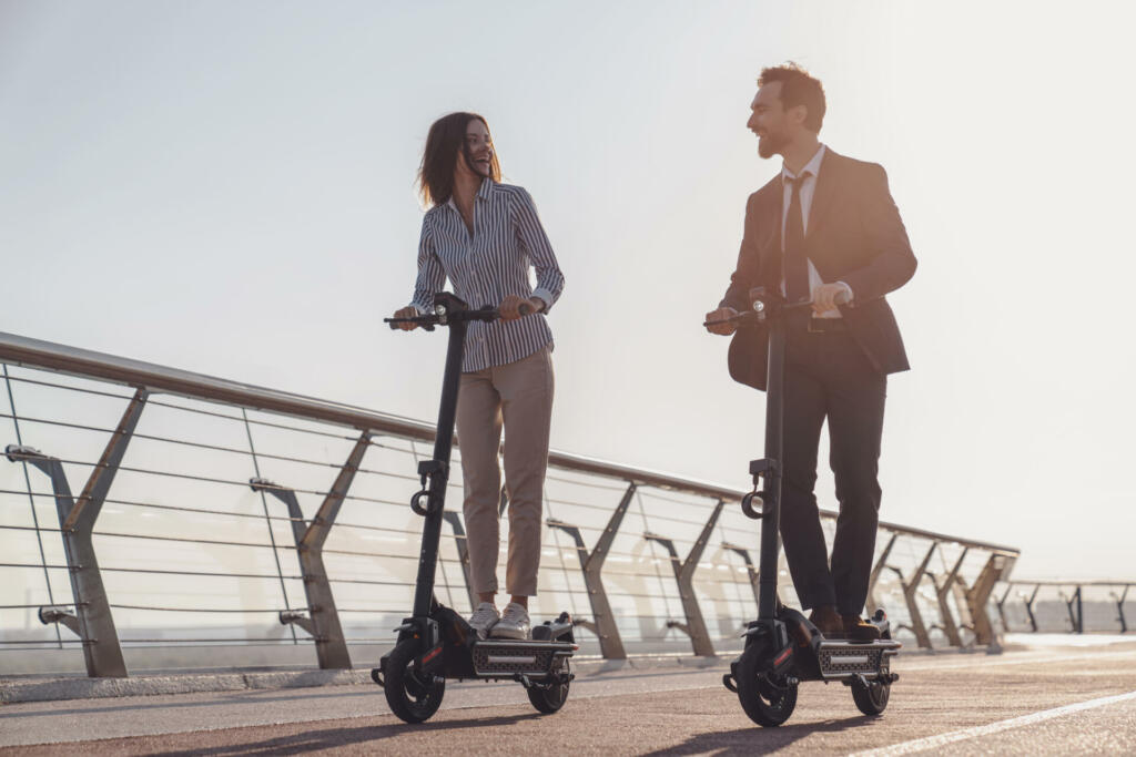 Young business man and business woman while riding electric scooters on the background of the morning city