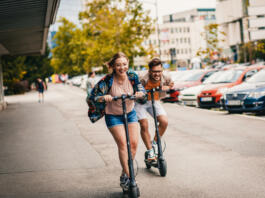 Young couple on vacation having fun driving electric scooter through the city.