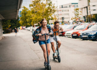 E-skiroji bodo »in« naslednjo pomlad Young couple on vacation having fun driving electric scooter through the city.
