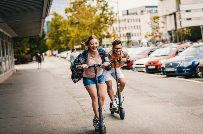 Young couple on vacation having fun driving electric scooter through the city.