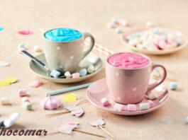 Modra in roza vroča čokolada v skodelicah, po mizi so potresene sladkorne penice
