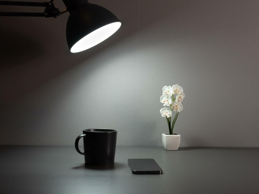 A table lamp illuminates a cup of coffee and a phone. A cup of coffee and a telephone on a gray table.