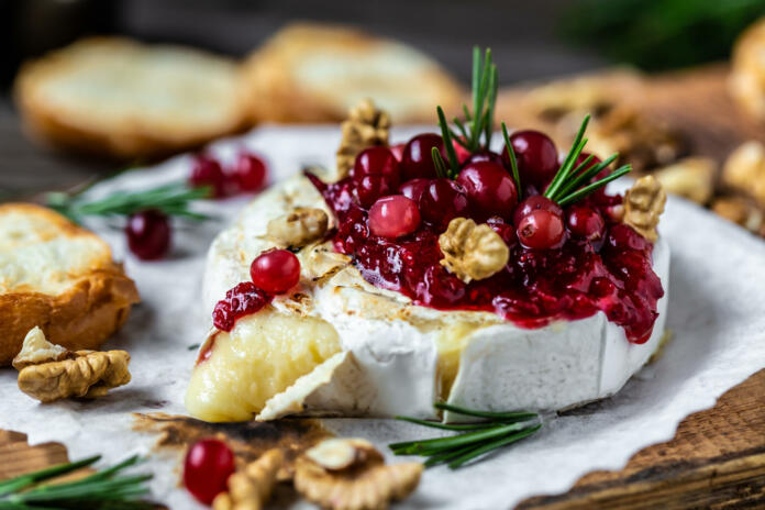 Baked Camembert brie with fresh rosemary and cranberry sauce. Gourmet appetizer. Breakfast, Food recipe background. Close up