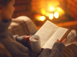 book and cup of coffee in hands of girl on winter autumn evening near fireplace