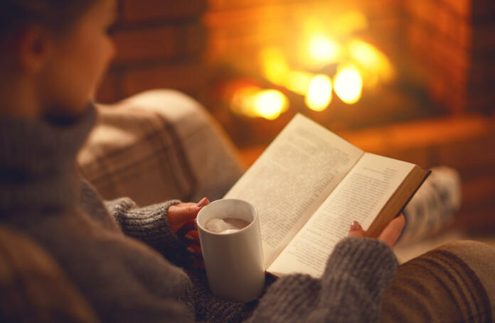 book and cup of coffee in hands of girl on winter autumn evening near fireplace