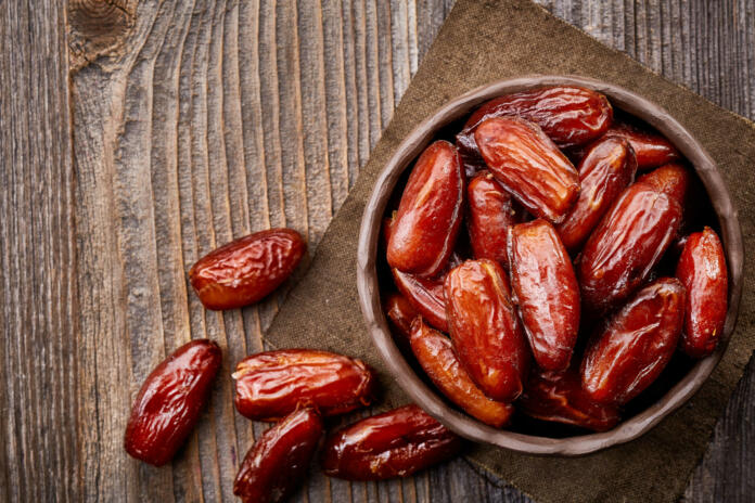 Bowl of dried dates on wooden background from top view