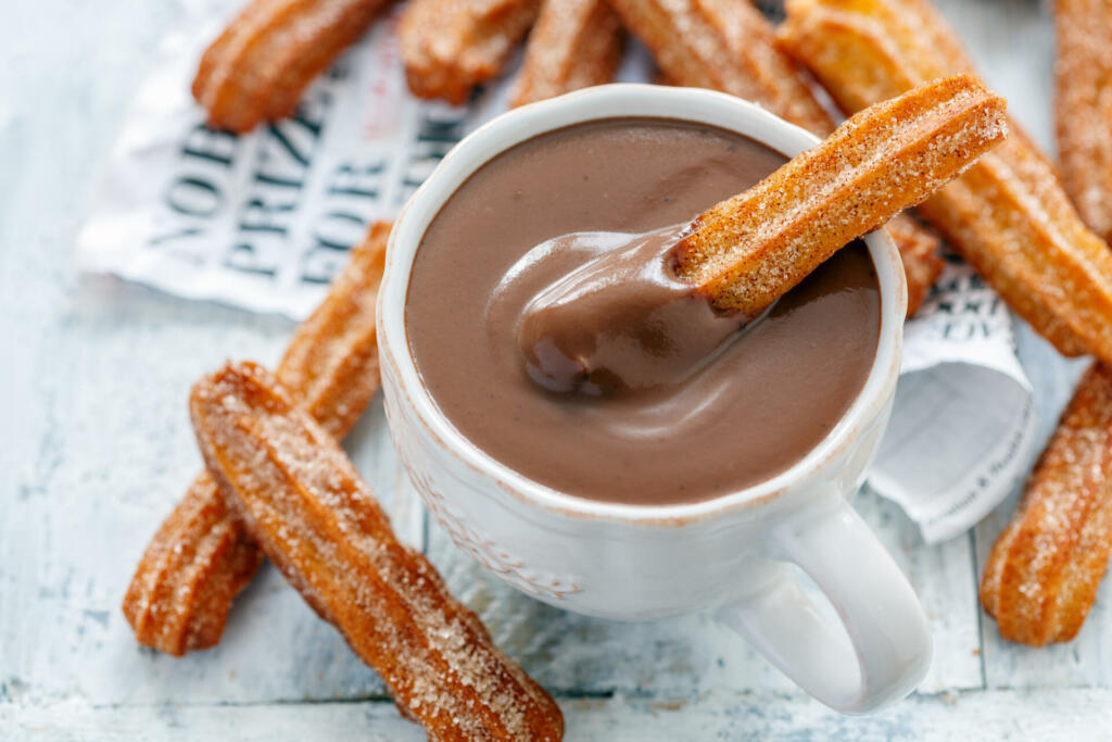 Churros with a cup of hot chocolate closeup, selective focus.
