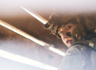 Vloga žensk v mirovnih operacijah Close up view through hole of wood wall of beautiful soldier woman with combat suit look to the camera.