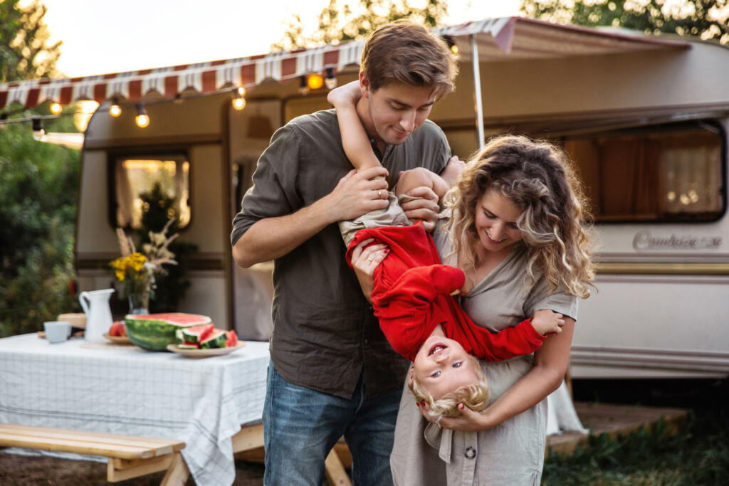 Family vacation: young parents enjoy bonding with little son camping in woods travel on caravan rv car. Happy mom and dad have fun outdoor camper trailer with kid on sunset. Recreation relax concept