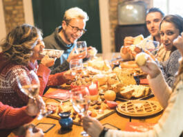 Front view of friends group tasting christmas sweets food and having fun at home drinking champagne sparkling wine - Winter holidays concept with people enjoying time eating together - Warm filter