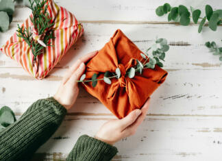 Med mladimi vse bolj priljubljen »no-gift December« Furoshiki tissue wrapping of presents. Female hand holding a gift in eco friendly reusable fabric package. Small business, ethical shopping idea. Presents packed in plastic free. Zero waste lifestyle