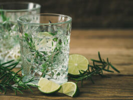 Glasses with a refreshing lime rosemary drink, lime halves and rosemary branches on old wood